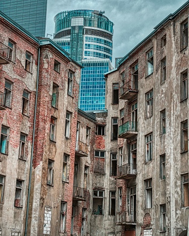 The modern buildings and skyscrapers behind old dirty apartment buildings - the contrast of new and old