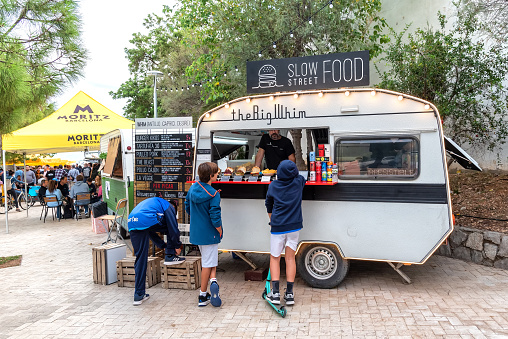 Sitges, Barcelona, Spain - October 08, 2022:  Children talk to fast food vendor in caravan set up for street vending.