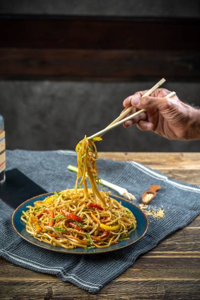 istock Vertical view of a hand picking Chinese noodles from the blue plate using chopsticks 1432509261