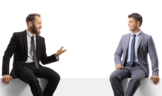 Two young professional men sitting on a panel and talking isolated on white background