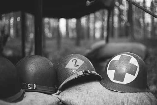 Metal Helmets Of United States Army Infantry Soldier At World War II. Helmets Near Camping Tent In Forest Camp. black and white photography