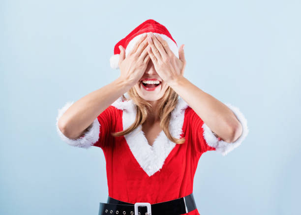 closeup of caucasian happy woman wearing santa clothes laughing closing her eyes closeup of caucasian smiling happy woman wearing santa clothes covering eyes with hands on blue solid background hair covering eyes stock pictures, royalty-free photos & images