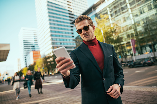 Successful businessman in full suit using smart phone for video call or to call taxi