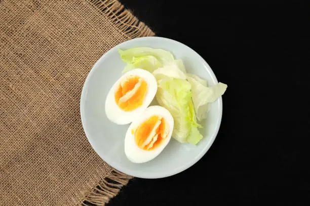 Halves of a hard boiled chicken egg with lettuce on a plate on a dark background - top view