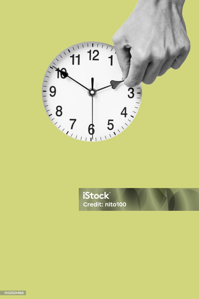 man resets a clock backward or forward the hand of a young man in black and white resets a clock backward or forward, at the end or at the beginning of the summer, on a green background with some blank space on the bottom Time Clock Stock Photo