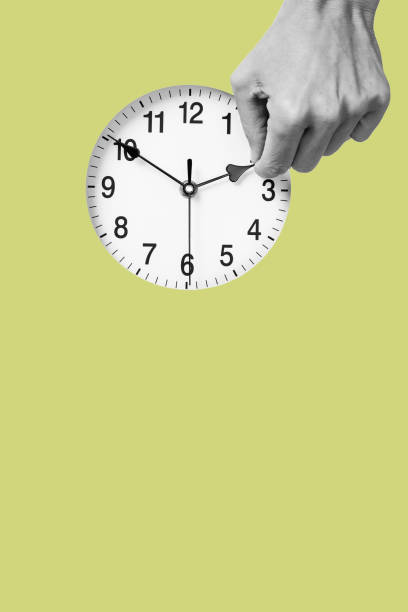 man resets a clock backward or forward the hand of a young man in black and white resets a clock backward or forward, at the end or at the beginning of the summer, on a green background with some blank space on the bottom hour hand stock pictures, royalty-free photos & images