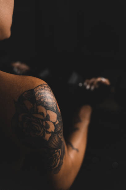 Young tattooed woman working out in the dark of her gym, preparing to do a cardio workout. Portrait of a young female athlete with short blond hair and tattoos in the gym. Determined young female kick boxer.