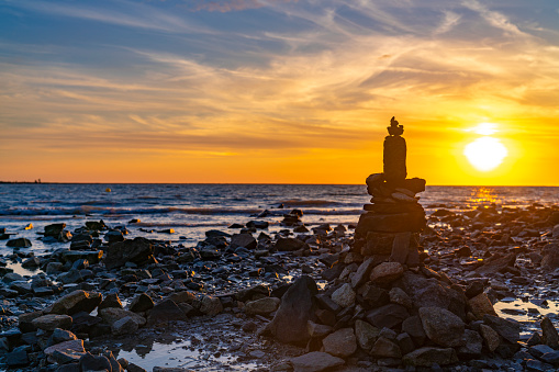 Cairn stacked stones in a sunset on the sea with horizon and golden blue sky on the dusk