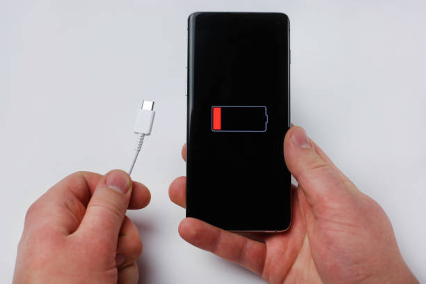 istock Holds charging cable and smartphone showing low battery 1432534983