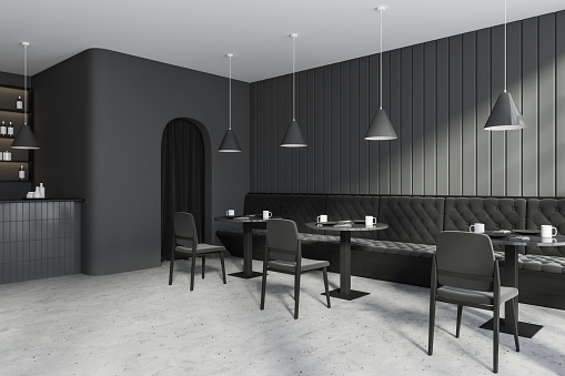 Corner view on modern dark cafe interior with grey walls, bar counter, tables with chairs and sofa, shelves with bottles, concrete floor. Concept of minimalist design. 3d rendering
