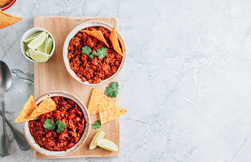 Chili con carne in bowls with tortilla chips on a gray marble background. Traditional dish of mexican cuisine. Top view with copy space