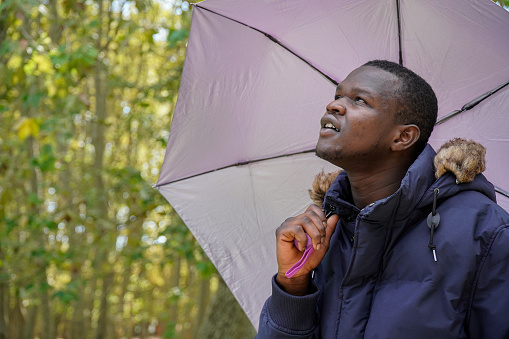portrait of a black male with a purple umbrella looking up.