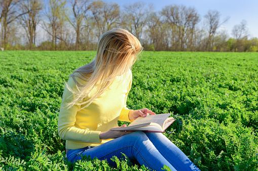 Blond woman reading a book in a green field