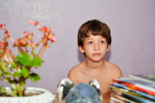 Kid sitting on chair with table against lilac wind television wall. Home on vacation. Salvador, Brazil.