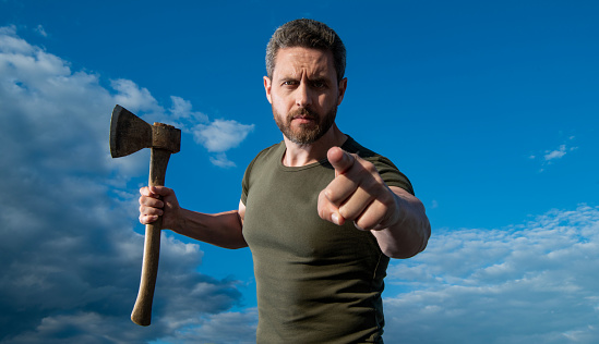 man threaten with axe. caucasian man hold ax. brutal man on sky background. point finger.