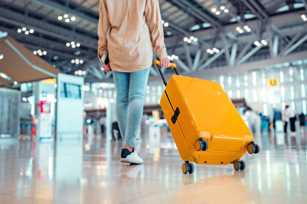 giovane viaggiatrice che cammina con una valigia gialla al moderno terminal dell'aeroporto, donna sulla strada per il gate d'imbarco del volo, pronto per il viaggio o il viaggio di vacanza - aeroporto foto e immagini stock