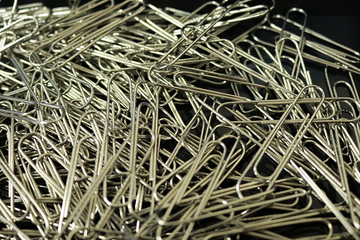 An abundance of silver paper clips on a white background with one colored paperclip in amongst the uniform silver ones.