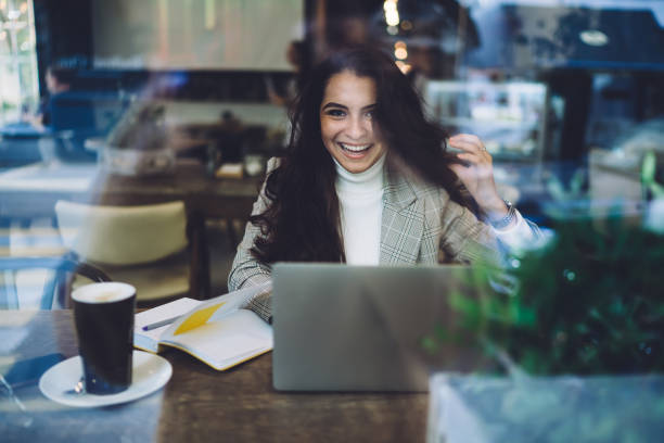 istock Portrait of happy hipster student sitting at desktop with knowledge textbook and laptop for e learning and smiling at camera, successful female freelancer working remotely with distance plan 1432552728