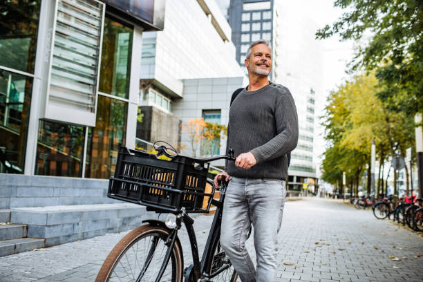 istock Handsome mature man riding cargo bicycle and contributes to eco-friendly environment. Businessman near green buildings 1432554124