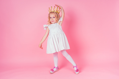 Beautiful queen in gold crown.little shopping girl in a princess fashion dress. Pretty child preparing for a birthday Easter party on a pink background in the studio.dancer ballerina.
