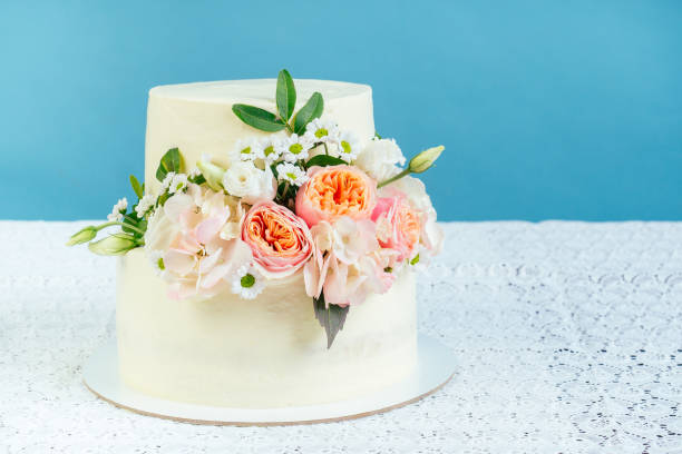 istock appetizing creamy white two-tiered wedding cake decorated with fresh flowers on a table with a lace tablecloth in studio on a blue background 1432555087