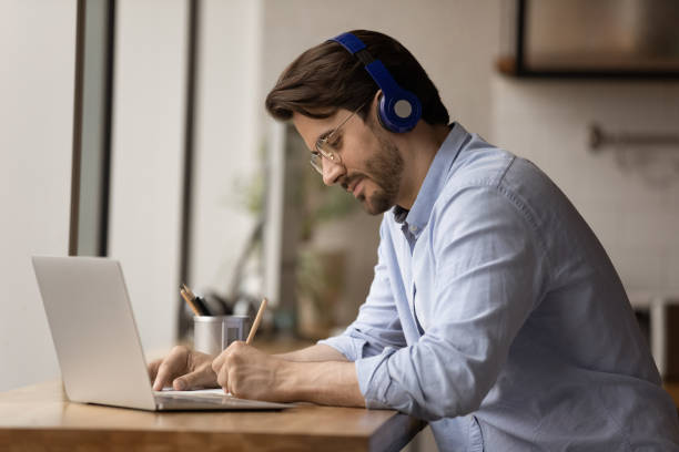 istock Diligent man student in earphones answering test questions on paper 1432556752