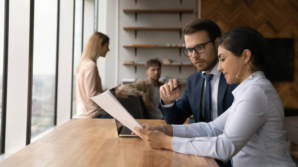 istock Two diverse teammates mentor intern discuss documents at coworking area 1432556774