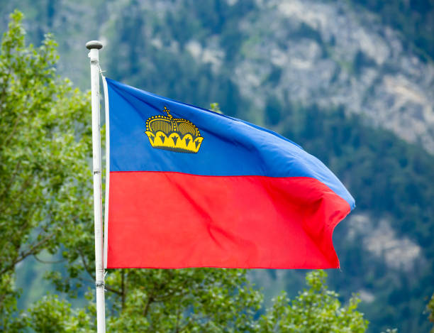 Blue and red national flag of Principality of Liechtenstein waving on flagpole on mountains background on summer