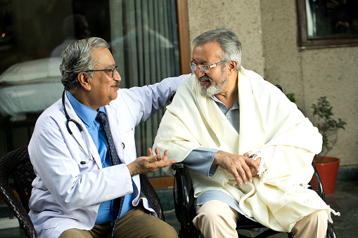 Male doctor discussing with disabled patient on wheelchair at home