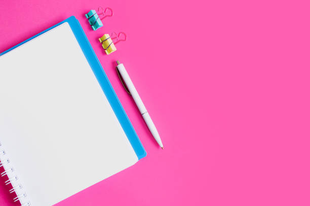 istock Notebook, pen, paper clips on a pink background, flat lay, top view, copy space. Office table desk, female workplace 1432566692
