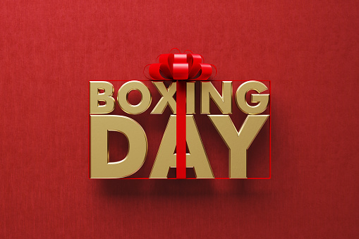 Gold colored Boxing Day word wrapped by red ribbon on red background. Directly above. Horizontal composition with copy space. Great use for Boxing Day concepts.