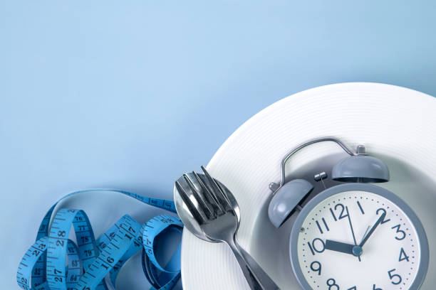 measuring tape with dish and spoon decoration on a blue background , intermittent fasting dieting concept stock photo