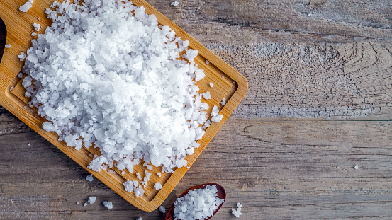Top view of salt crystals in wooden spoons on old wooden background.Salt flavored condiment salt.