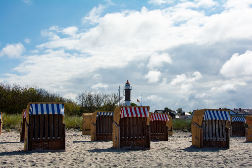View of brown traditional wicker beach baskets  chairs and the lighthouse on the sandy beach at the Baltic Sea, near Timmendorf Strand, on the island of Poel, Germany