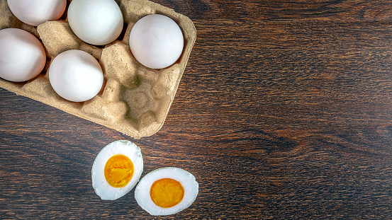 Top view of  duck eggs in an egg box and duck egg is cut in half to reveal the yolk on wooden background