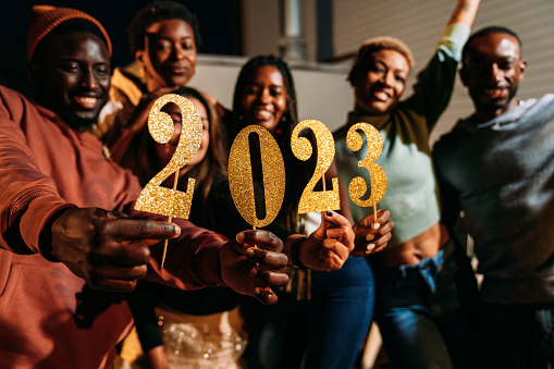 Friends are holding the number 2023 to celebrate the New Year's Eve. Night party on a rooftop in New York.