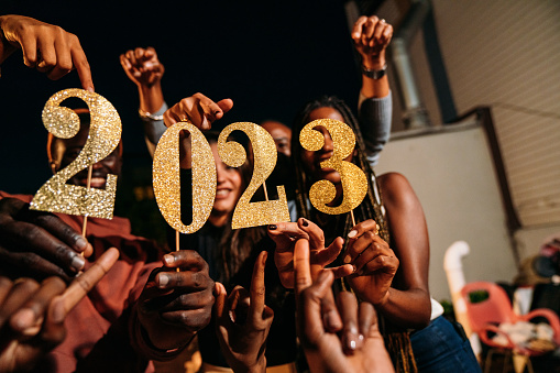 Friends are holding the number 2023 to celebrate the New Year's Eve. Night party on a rooftop in New York.
