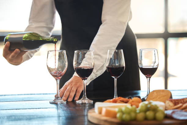 Luxury, fine dining and hospitality with a waiter pouring red wine at a restaurant. Preparing for a wine tasting with a professional sommelier, good service with quality drink by a male winemaker Waiter pouring red wine in wineglass, preparing for a wine tasting at a restaurant with a professional sommelier. Fine dining and good service in the hospitality industry by a male winemaker restaurant food canapes appetizers stock pictures, royalty-free photos & images