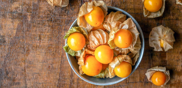 vue de dessus du fruit jaune mûr de la groseille du cap dans un bol en acier inoxydable sur fond en bois - cape gooseberries photos et images de collection