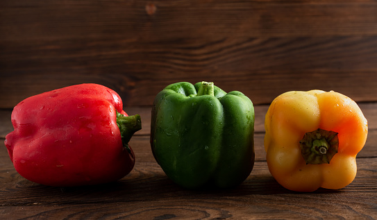 three peppers of different colors on a wooden background