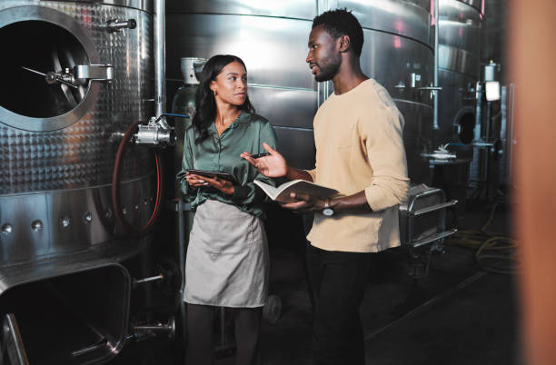 istock Wine production workers using alcohol machine or distillery equipment in warehouse winery. Business sommelier expert woman and man talking and working on quality control maintenance with a checklist 1432577211