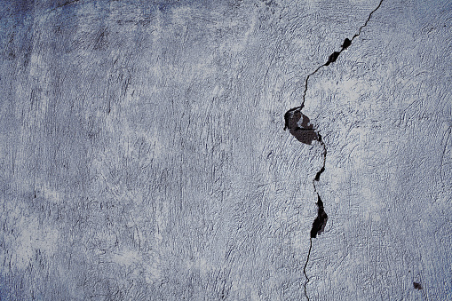 Cracked concrete wall with damaged surface, textured background.