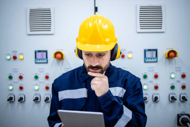istock Close up view of professional electrical engineer looking at digital tablet and standing by electric cabinets in factory. 1432579017