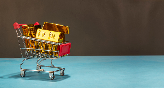 Shopping cart full of pure shiny gold bar or ingot on clean banner template