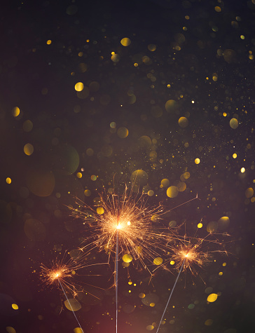 A pair of sparklers burn with a soft yellow light, scattering small stars of sparks around them