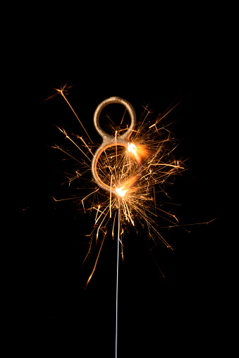 Burning golden sparkler in shape of number eight, digit 8, isolated on black background