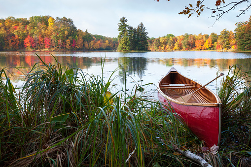 Red wooden canoe on shore of lake with trees in autumn color and a small island