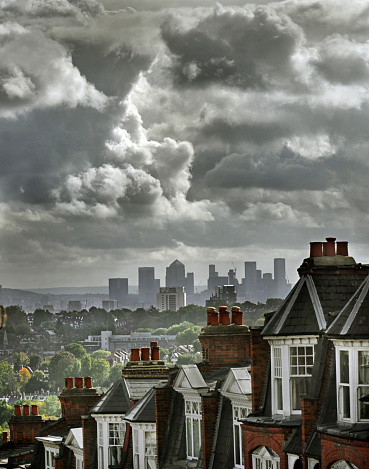 Period red brick home rooftops in a London suburban hill terrace overlooking the distant view of downtown  financial district offices. Looming storm clouds over the distant financial district London, UK