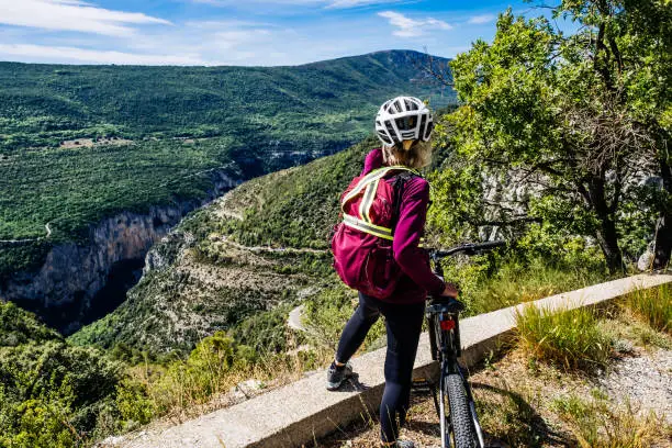 Mature female cyclist overlooking the Chalet de la Maline on the Route des Cretes at Verdon Gorge, Provence, France. Part of a series featuring all the main viewpoints.