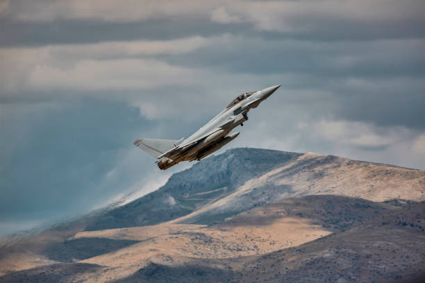 an Eurofighter Typhoon airplane climbing up towards sky in front of a hill